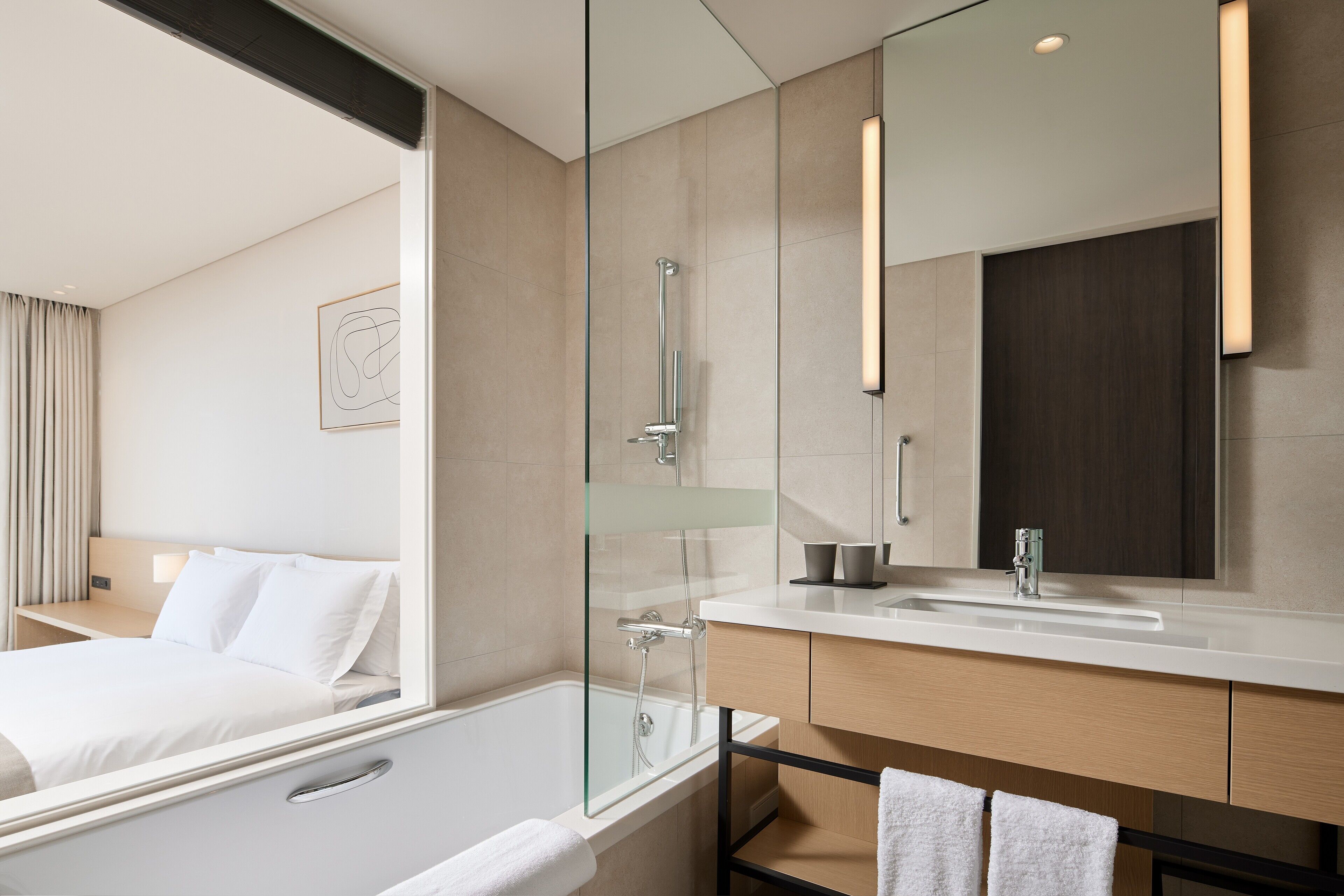 A modern hotel bathroom with a glass-enclosed shower, a white bathtub, a large mirror, and a white sink.