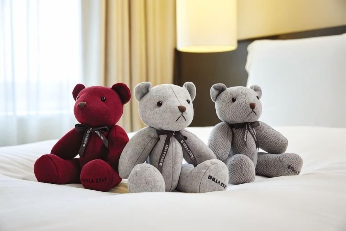 Three plush bears on a bed with a lamp in the background.