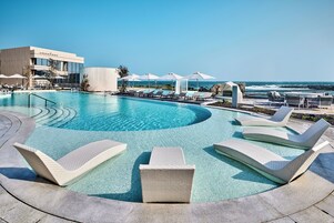 Zona de piscina con sillones de descanso y sombrillas, un edificio con el rótulo 'Wonderland' y vista al océano.