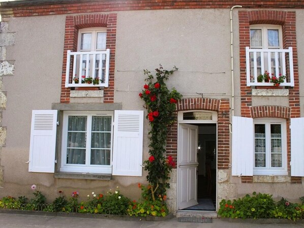 Un bâtiment à deux étages avec une façade en briques, des volets blancs et des jardinières aux fenêtres.