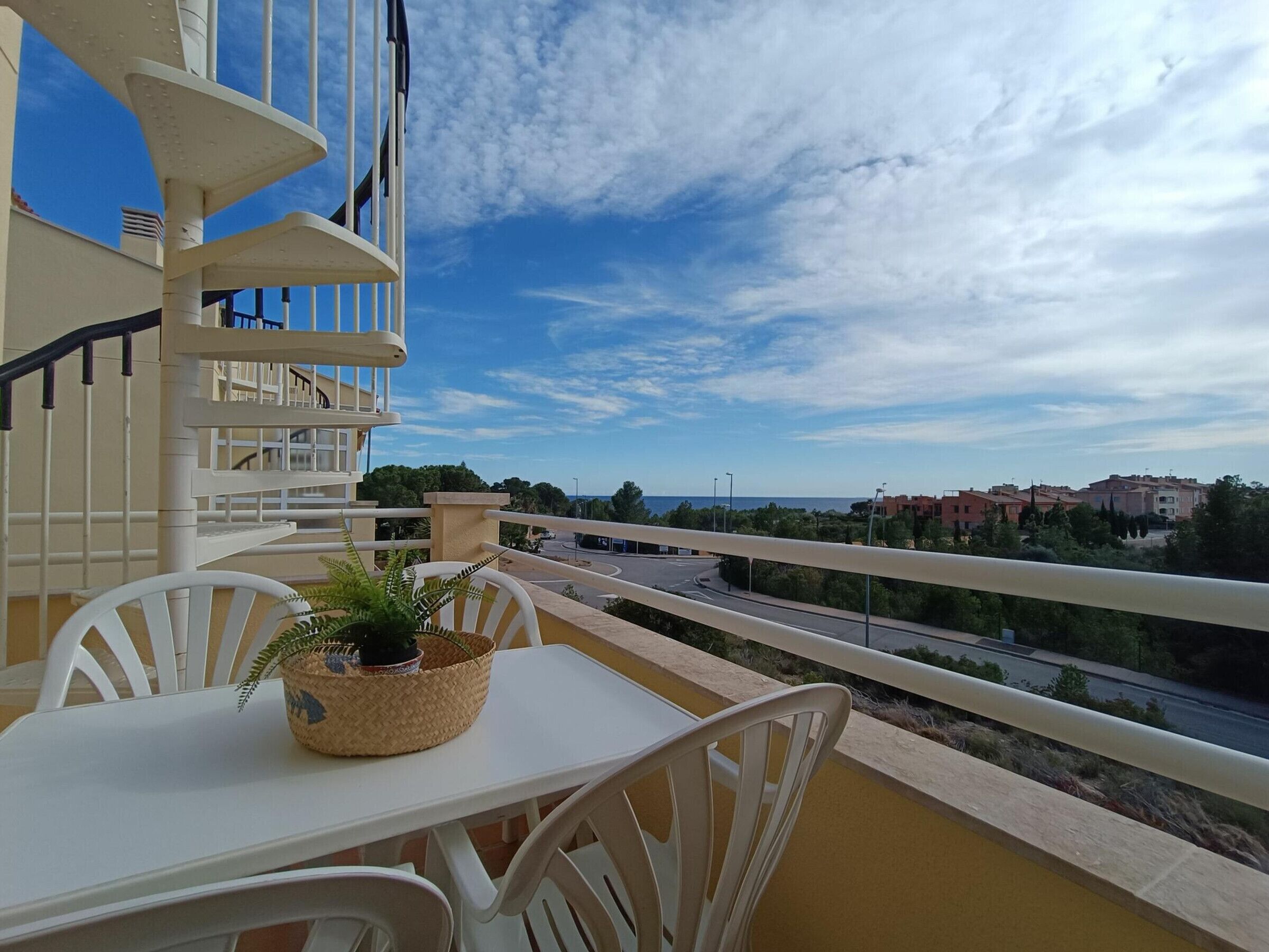 A balcony with a table and chairs, a potted plant, and a view of a road and buildings.