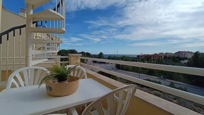 Een balkon met een tafel, stoelen, een bloempot en uitzicht op een weg en gebouwen.