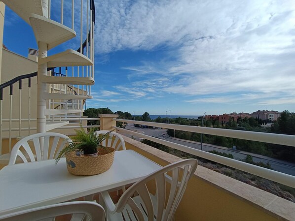 A balcony with a table and chairs, a potted plant, and a view of a road and buildings.