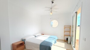 Een slaapkamer met twee bedden, een plafondventilator, een raam en een houten plank.