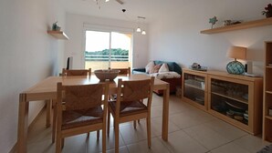 Een eethoek met een tafel, stoelen, een plafondventilator, een bank, een kast met glazen deuren en uitzicht door een groot raam.