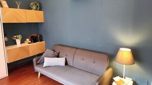 A modern living room with a grey sofa, wooden shelves, a lamp, and a small table with a book. - Gaia Suites  (Turin)