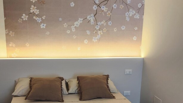 A bedroom with a large floral tapestry on the wall, a bed with two pillows, and a bedside table. - Gaia Suites  (Turin)