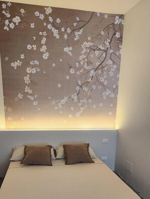 A bedroom with a large floral tapestry on the wall, a bed with two pillows, and a bedside table. - Gaia Suites  (Turin)