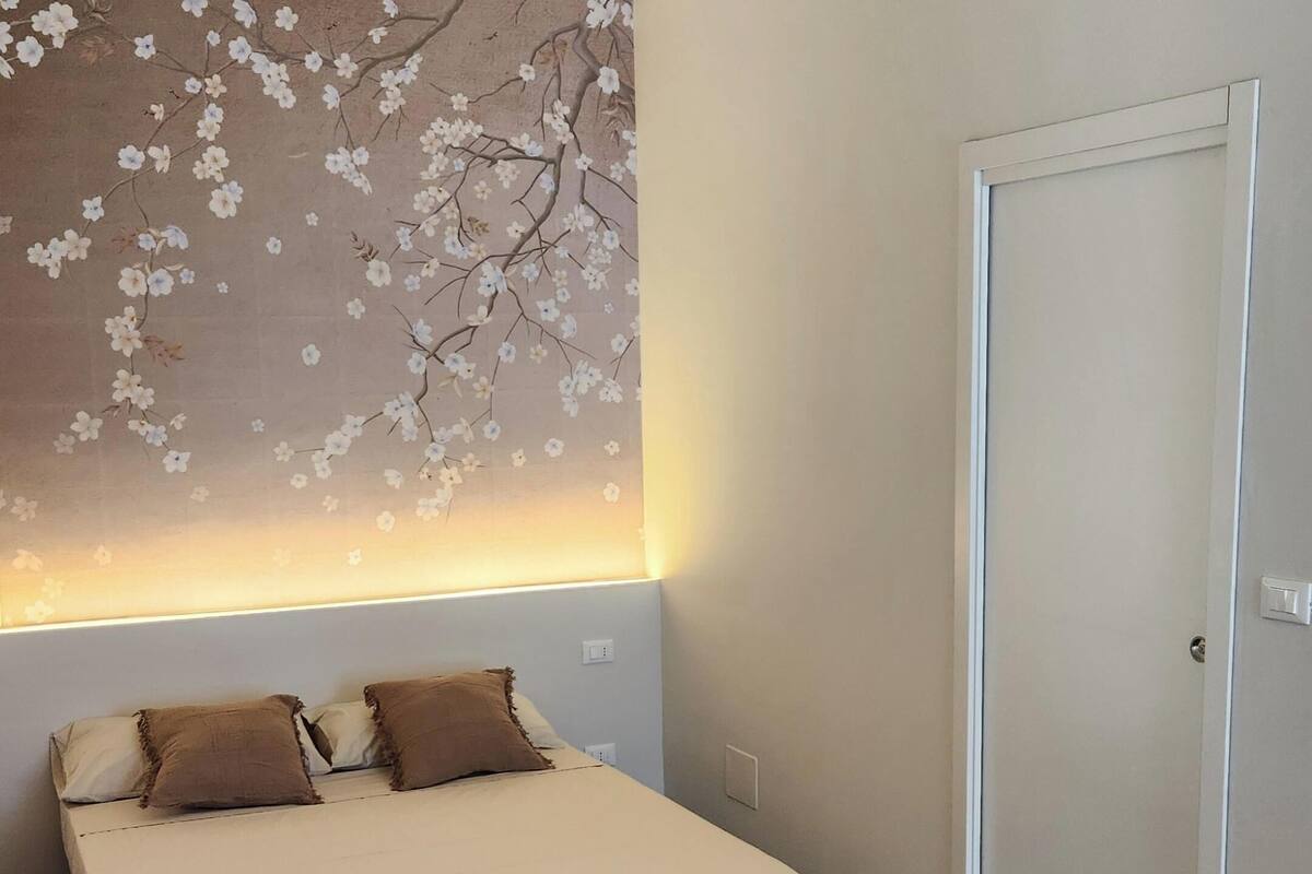 A bedroom with a bed, a nightstand, a wall-mounted light, a door, and a tiled floor.