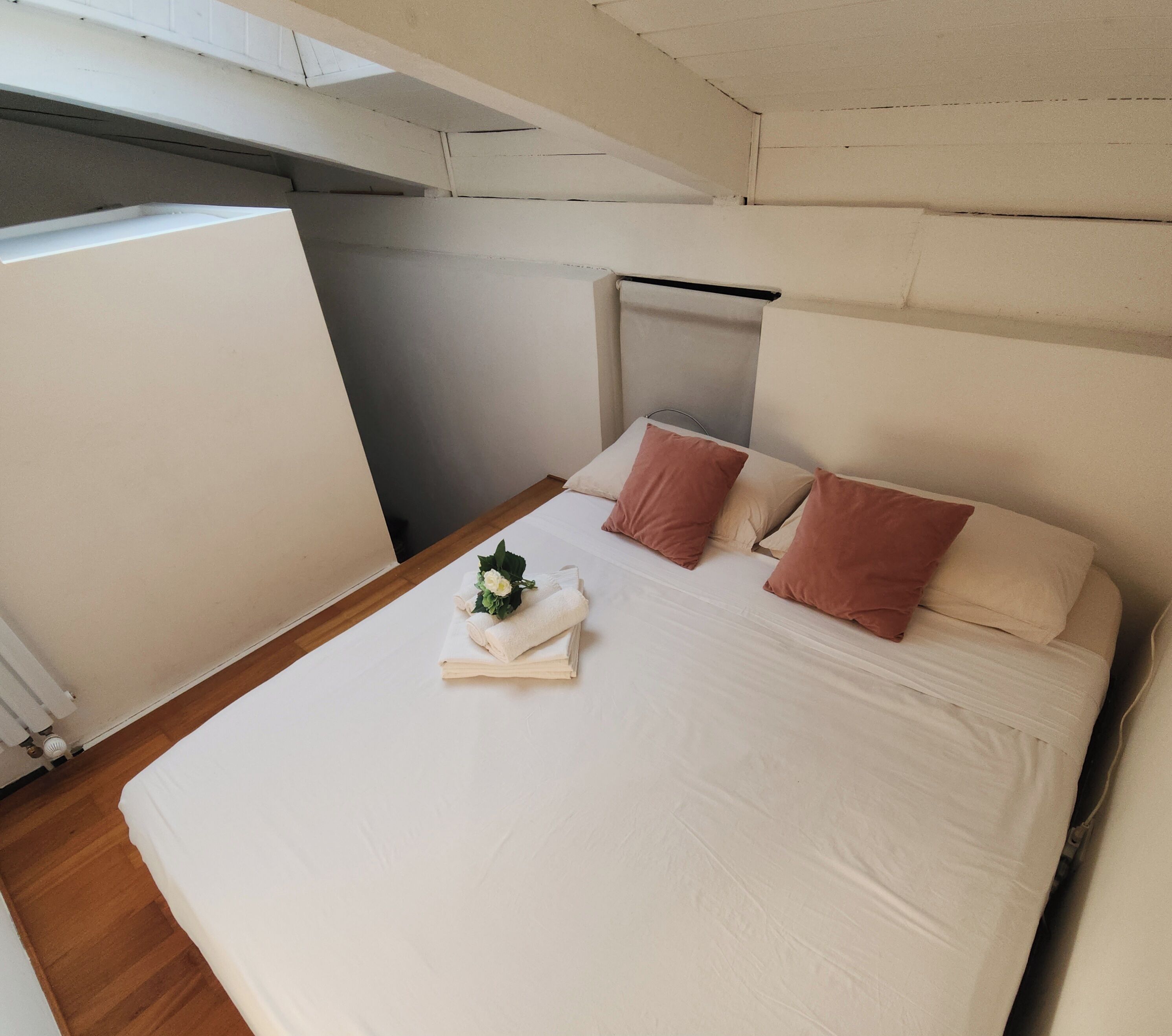 A neatly made bed with white and brown pillows, a folded white towel, and a small bouquet of flowers.