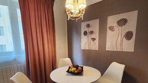 A dining area with a round table, two white chairs, a fruit bowl, a chandelier, and wall art. - Gaia Suites  (Turin)