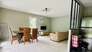 Un salón espacioso con mesa de comedor, sillas, sofá, televisor y una zona de cocina con refrigerador.