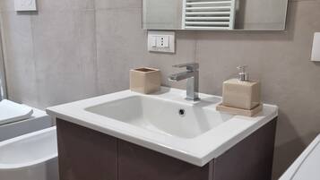 Un baño con un lavamanos blanco, un espejo encima y un perchero para toallas.