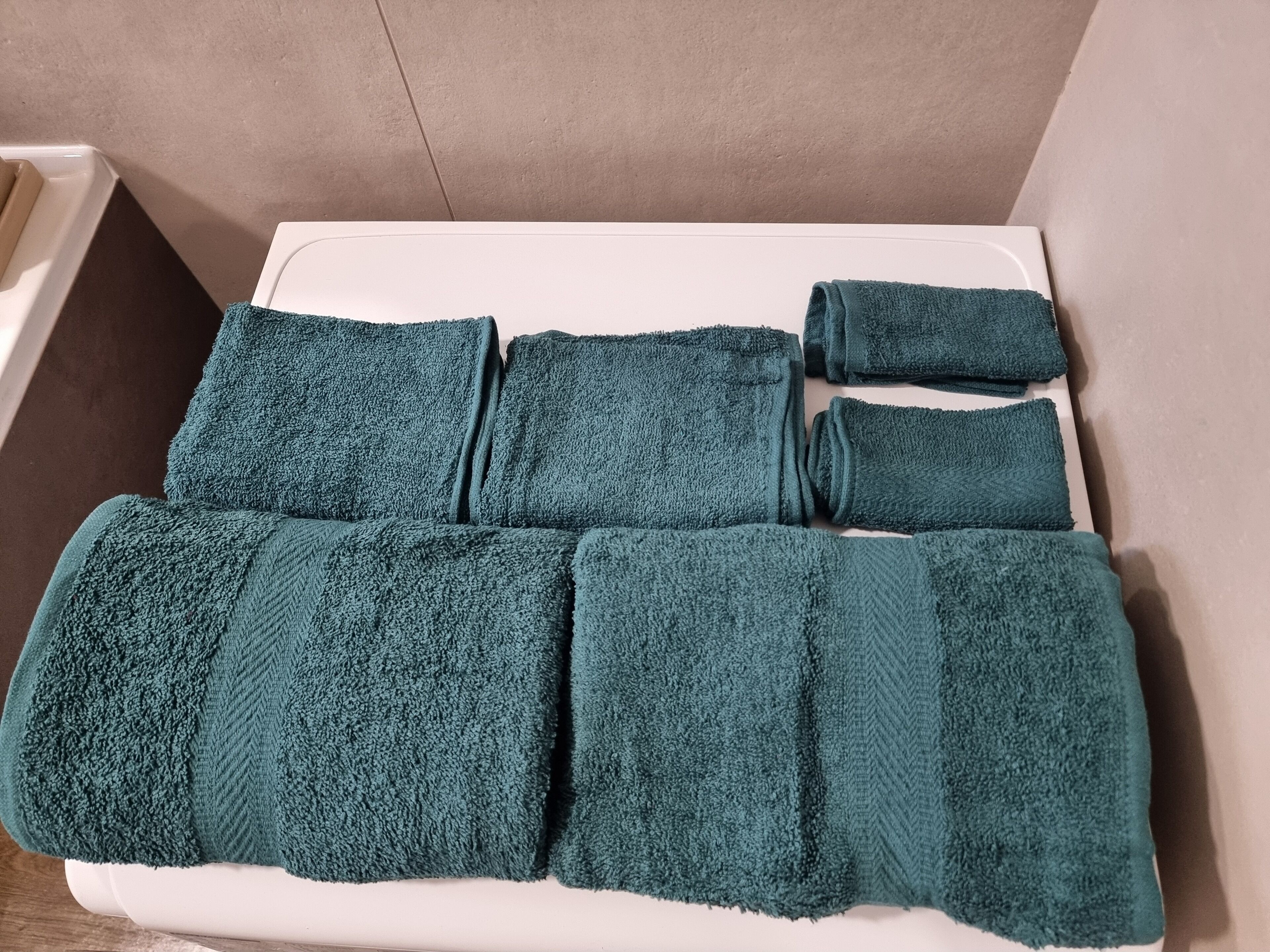 A white bathtub with six teal towels neatly folded and stacked on top.