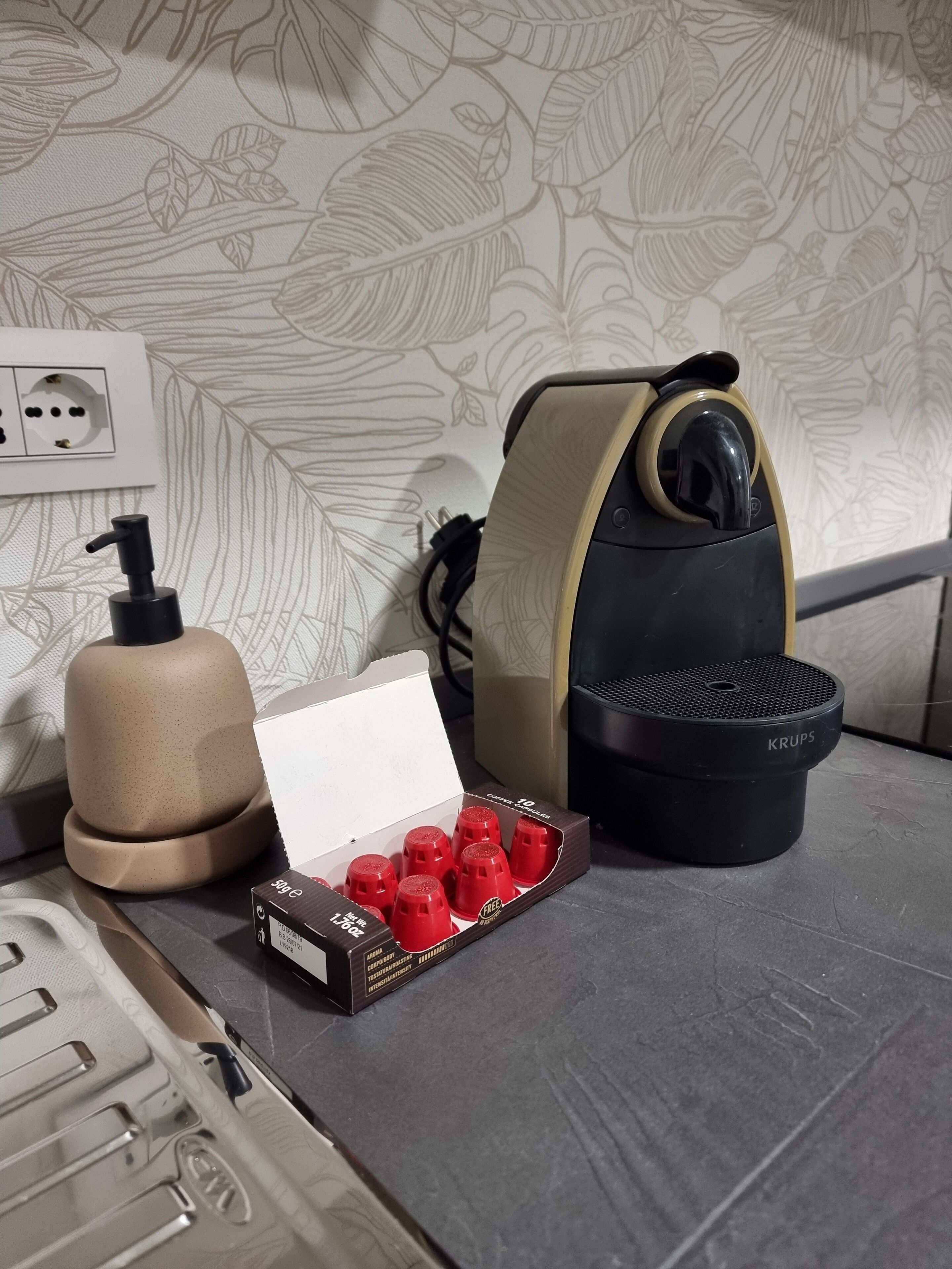 A kitchen counter with a coffee machine, a bottle of hand soap, and a box of red peppermints.