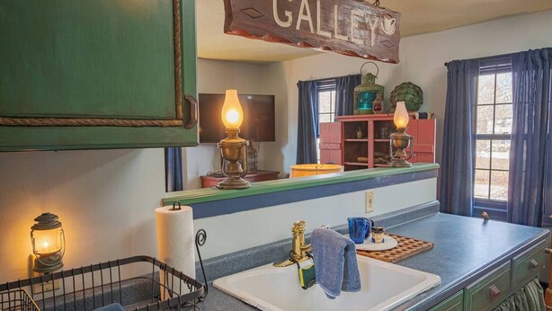 Una cocina con un letrero de madera que dice “THE GALLEY”, un fregadero, una estufa y una ventana con cortinas.
