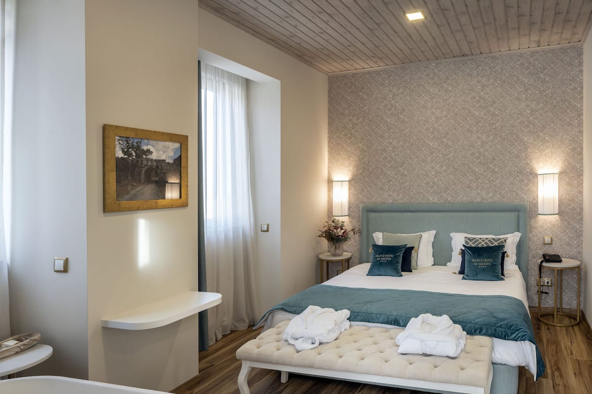 A hotel room with a large bed, bedside tables, a bench, and a bathtub.