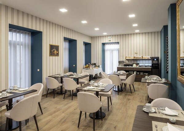 A hotel dining area with multiple tables and chairs, a kitchen in the background, and striped wallpaper. - Palace Hotel De Midões (Tábua)