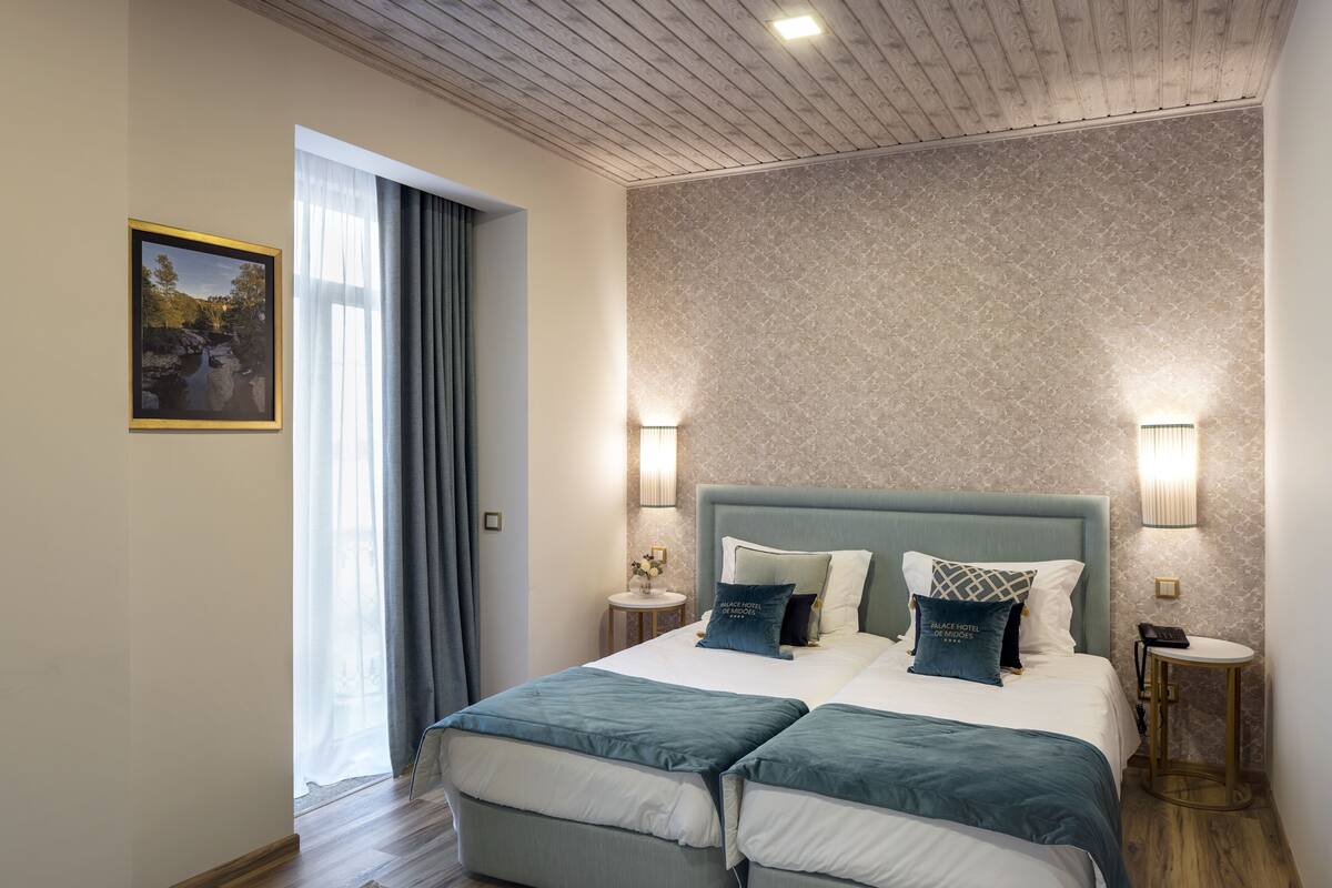 A modern hotel room with a large bed, two bedside tables, a nightstand, a wall-mounted lamp, and a framed picture on the wall.