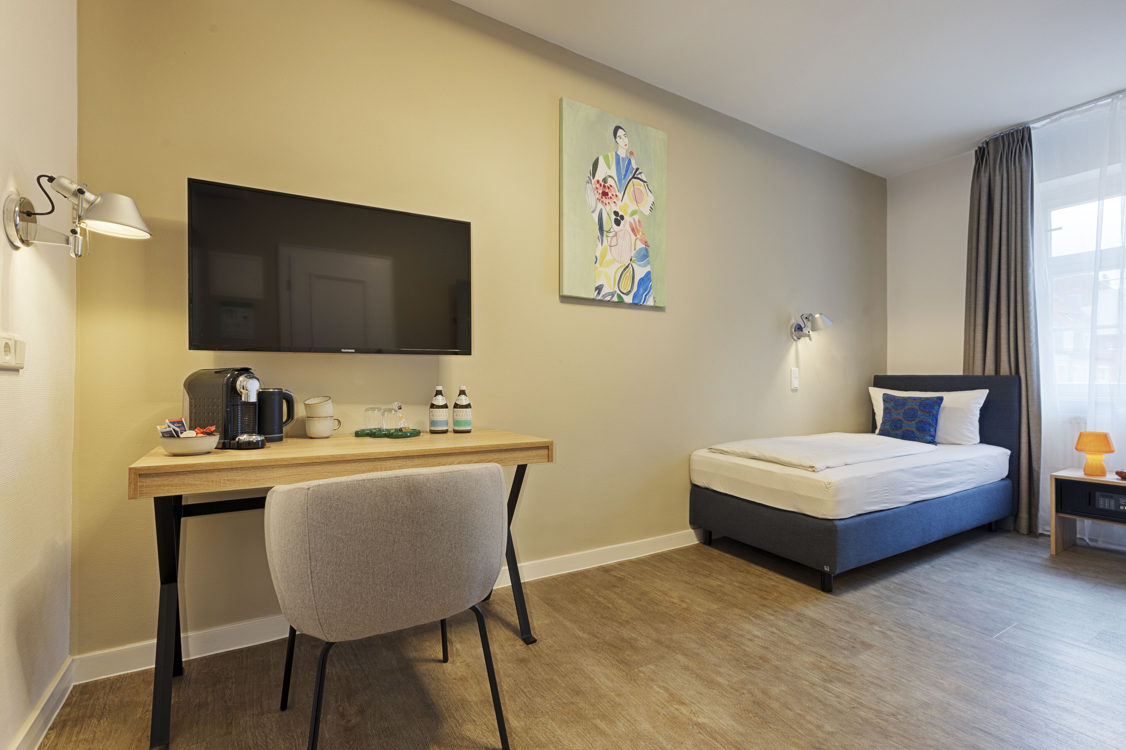 Ein Hotelzimmer mit Bett, Schreibtisch mit Stuhl, Fernseher und einem Bild an der Wand.