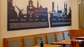 A restaurant interior with wooden tables and benches, hanging pendant lights, and cityscape wall art. - homie hotel zur stadt mainz (Würzburg)