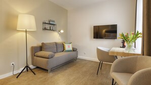 A modern living room with a sofa, a floor lamp, a coffee table, and a TV mounted on the wall. - homie hotel zur stadt mainz (Würzburg)
