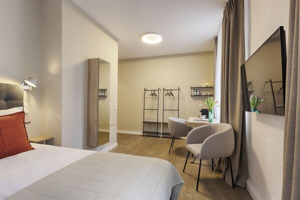 A hotel room with a bed, a desk, a chair, a wardrobe, and a mirror.