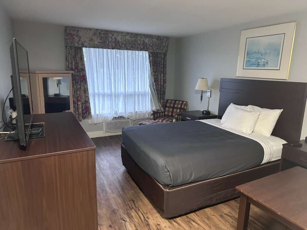 A hotel room with a large bed, a desk, a chair, a lamp, and a window with curtains.