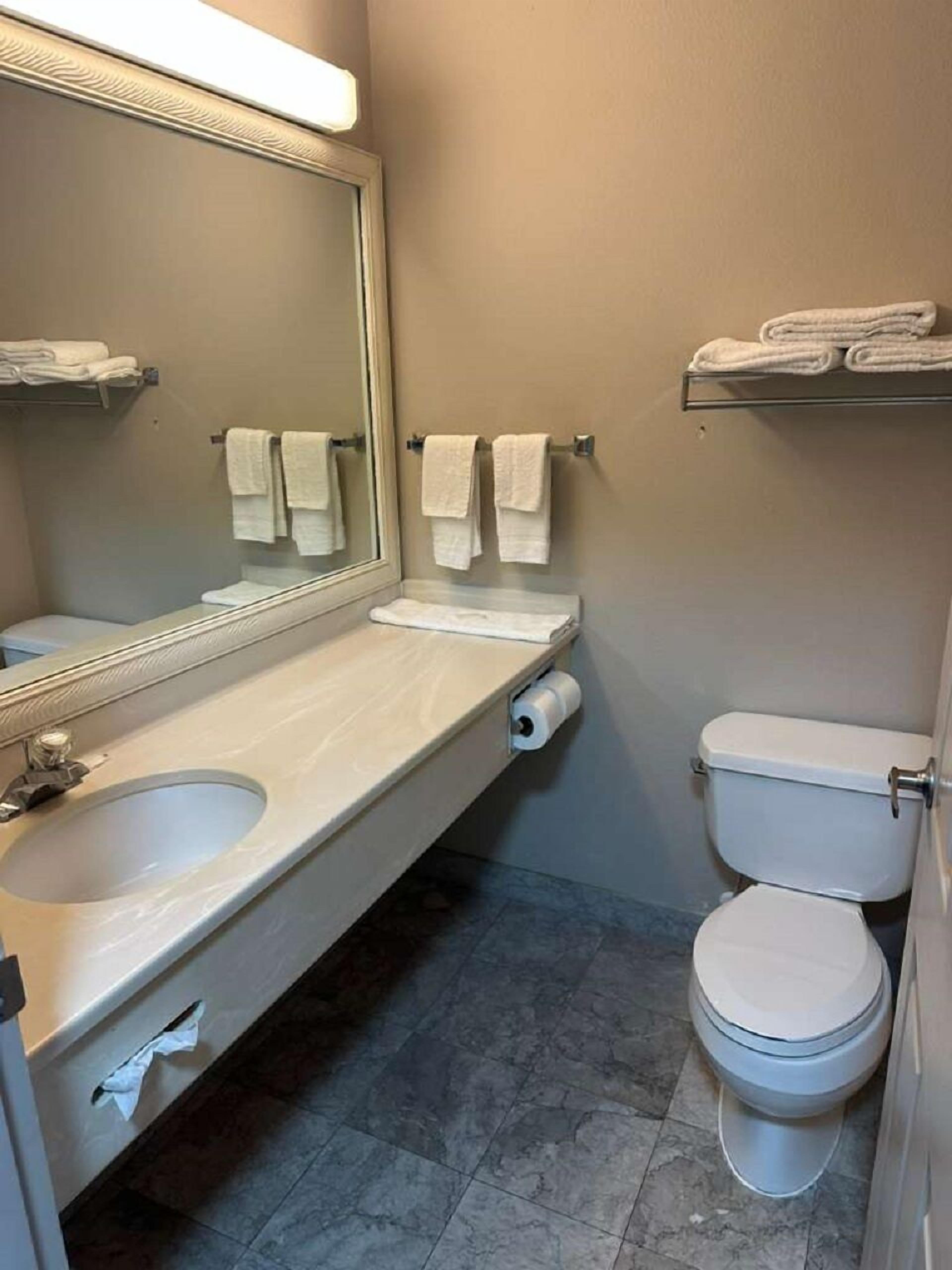 A bathroom with a sink, mirror, towel rack, toilet, and a shelf with folded towels.