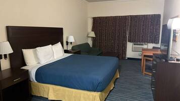 A hotel room with a large bed, a desk with a chair, a lamp, and a window with curtains.