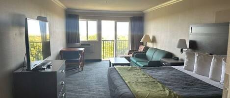 A hotel room with a bed, a desk, a chair, a TV, and a balcony with a view.