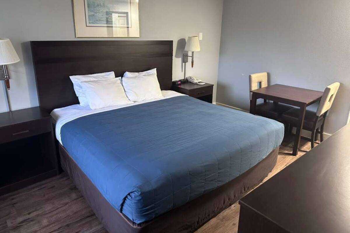 Une chambre d’hôtel avec un grand lit, un bureau, une chaise, une table de chevet, une lampe et un tableau encadré au mur.