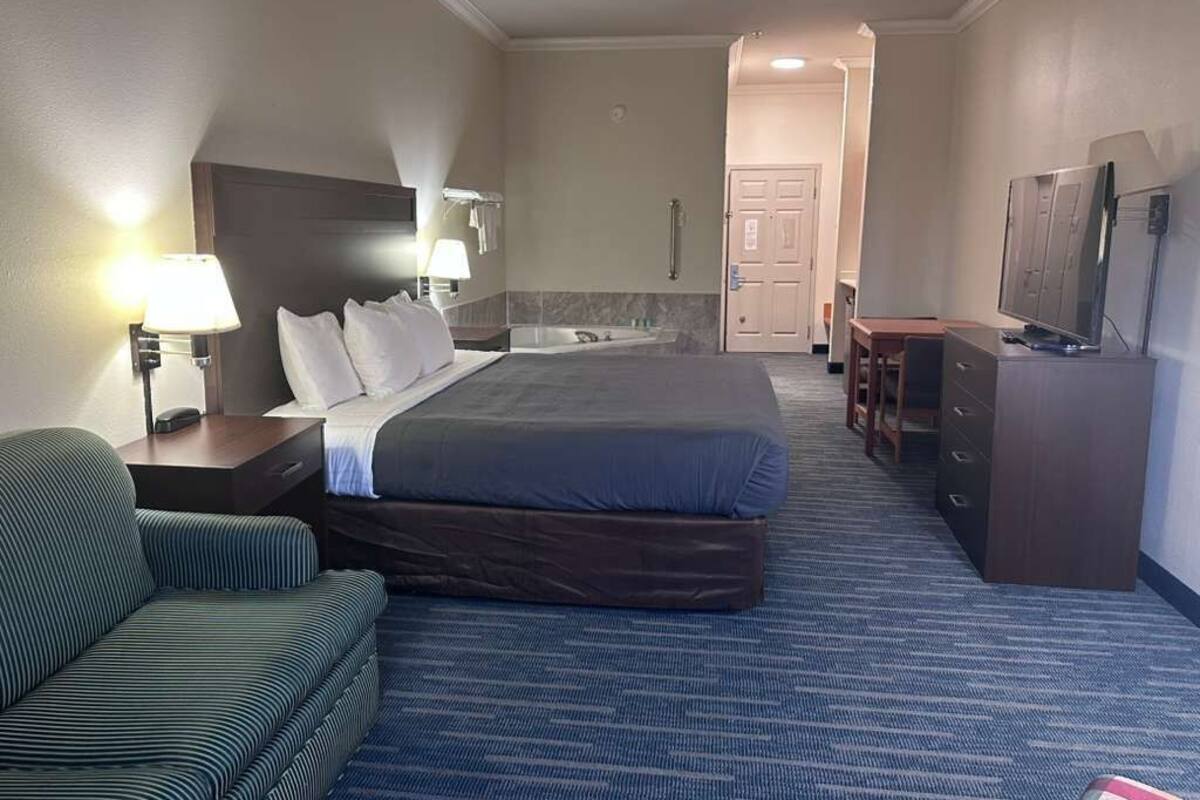 Une chambre d’hôtel avec un lit, un bureau, une chaise, une télévision et une salle de bain visible au fond.