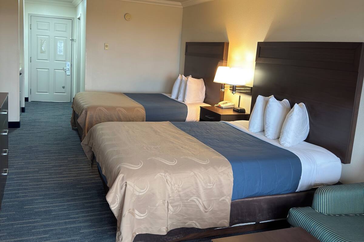Une chambre d’hôtel avec deux lits, un bureau, une chaise et une lampe.