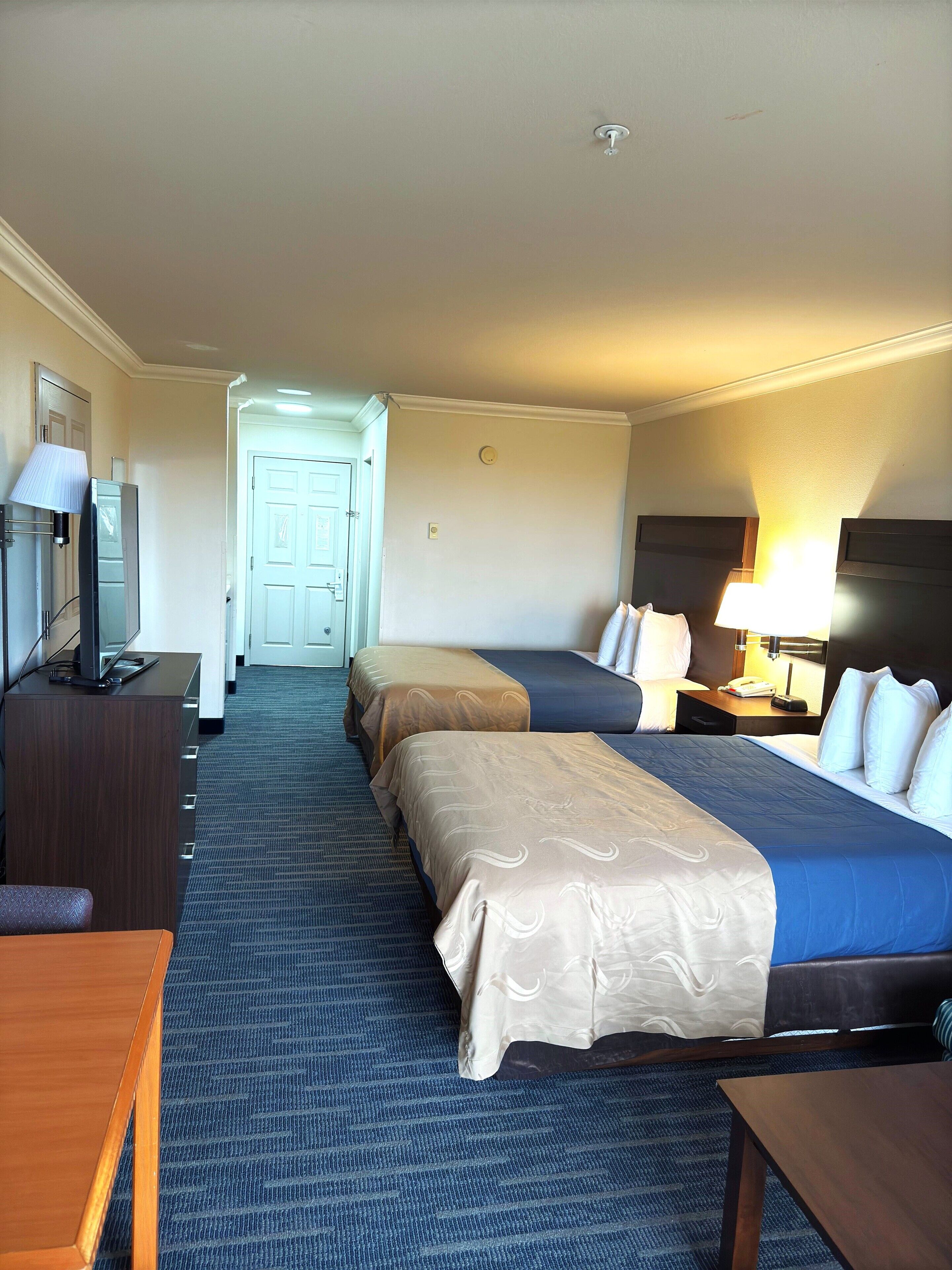A hotel room with two beds, a desk, a TV, and a lamp.
