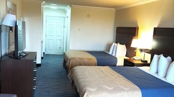 A hotel room with two beds, a desk, a TV, and a lamp.