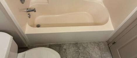 Un baño con bañera, inodoro y piso de baldosas.