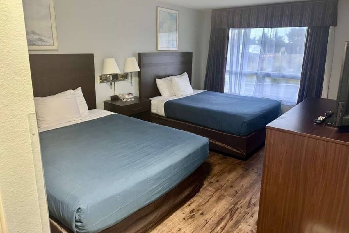 Une chambre d’hôtel avec deux lits, un plancher en bois, un bureau et une fenêtre avec des rideaux.