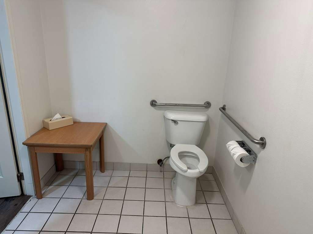 Ein kleines Badezimmer mit Toilette, einem Holztisch und einer Handstange.