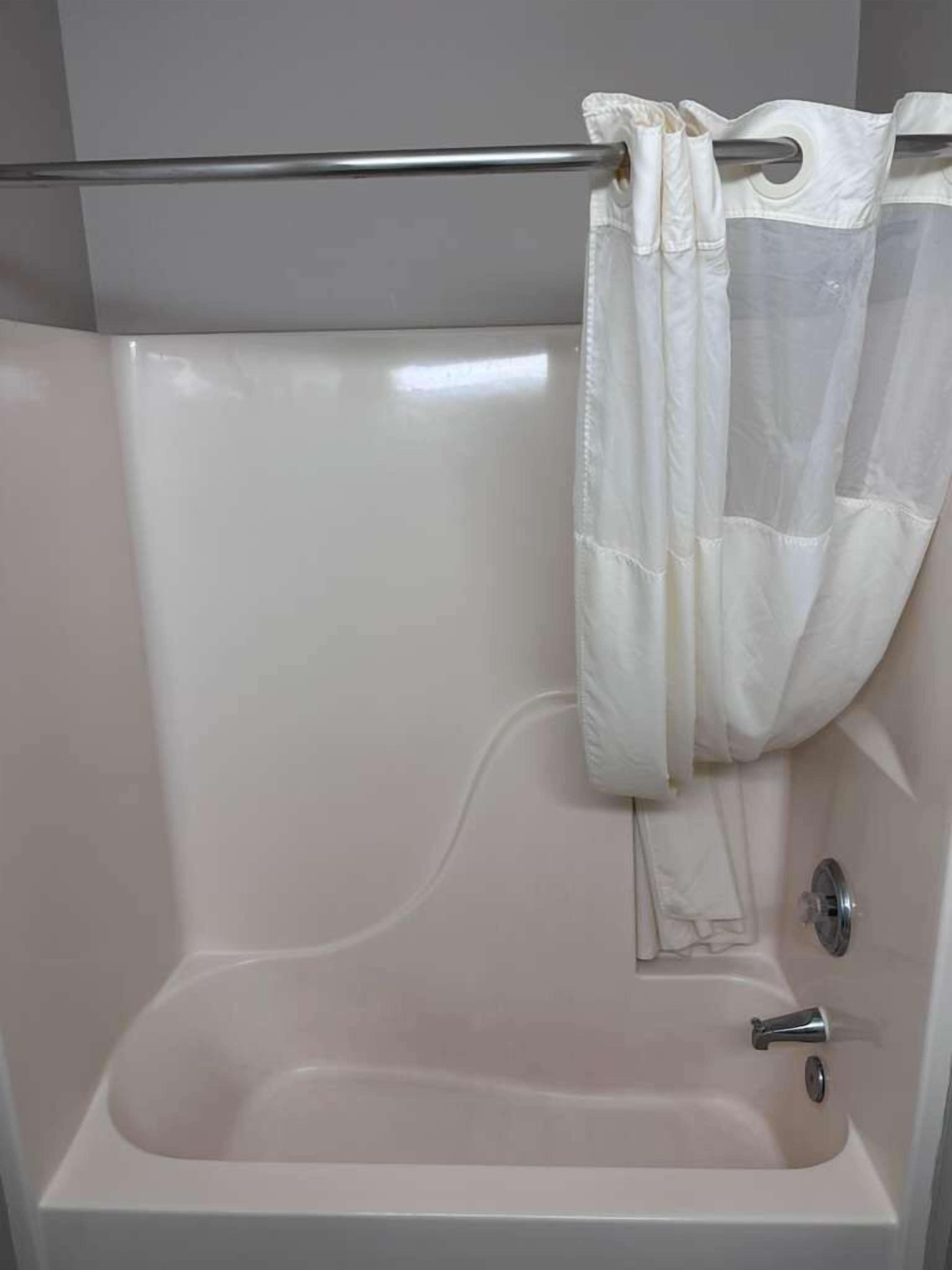 A standard bathtub with a faucet and a shower curtain rod.