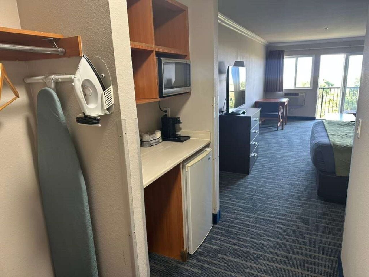 A hotel room with a kitchenette, a desk, a bed, and a view of the outdoors.