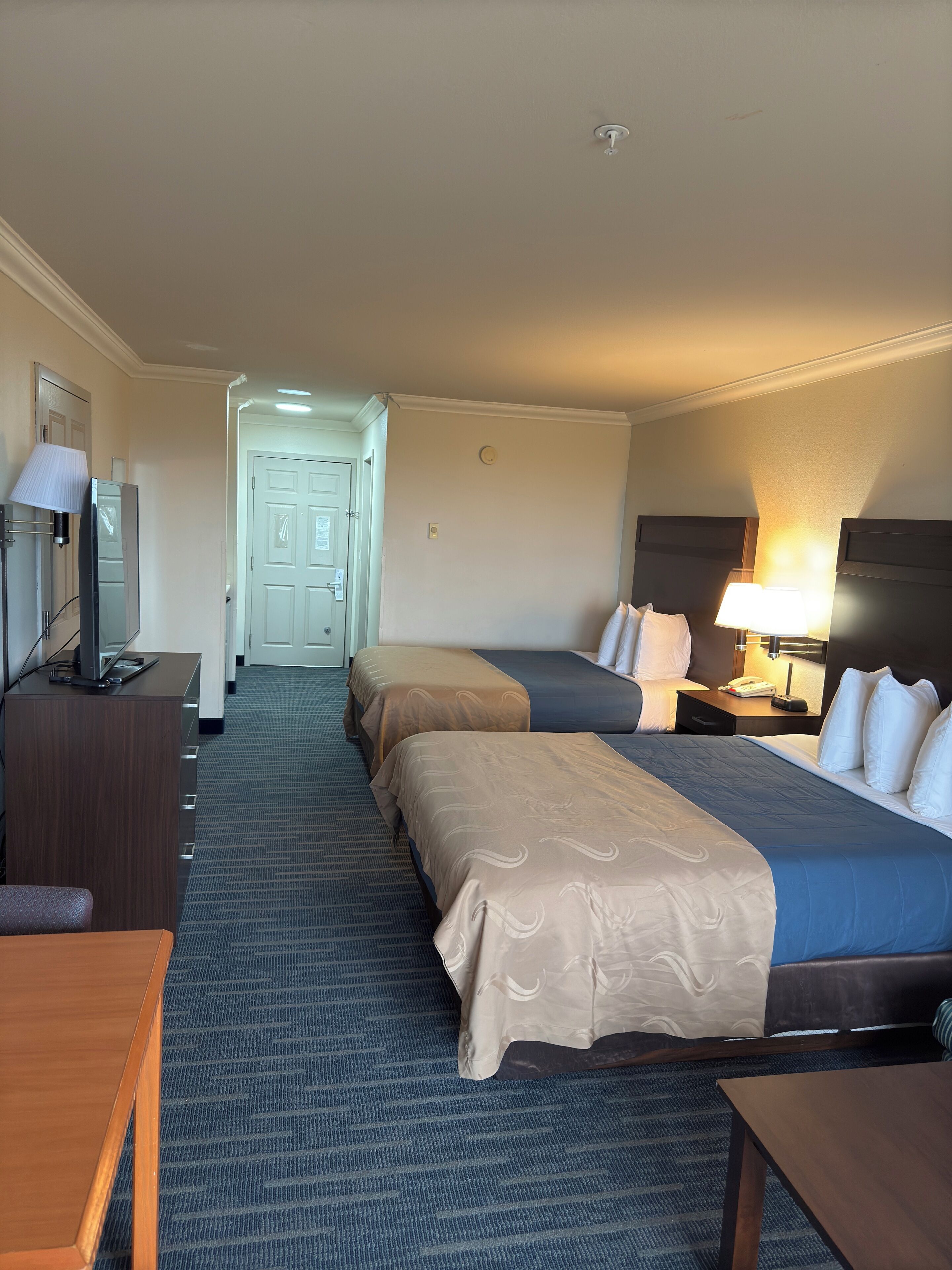 A hotel room with two beds, a desk, a TV, and a lamp.