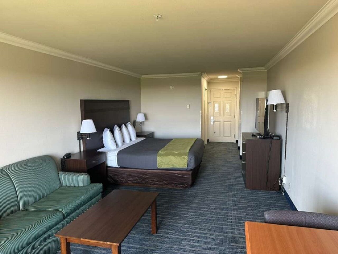 A hotel room with a bed, a green sofa, a wooden table, a TV, and a lamp.