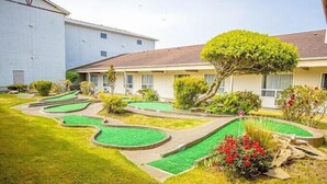 A residential property with a well-maintained lawn, a golf putting green, and a variety of shrubs and flowers.