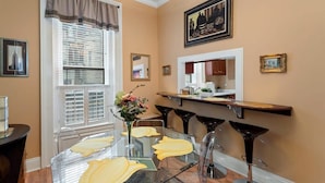 A dining area with a glass table, clear chairs, and a bar counter with stools. - The Louisville Cottage | Prime Location | Near DT! (Louisville)