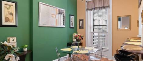 Un comedor con pared verde, una araña y una ventana con persianas.