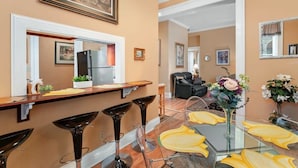 A modern kitchen with a refrigerator, a dining area with a glass table and bar stools, and a living room with a sofa and a coffee table. - The Louisville Cottage | Prime Location | Near DT! (Louisville)