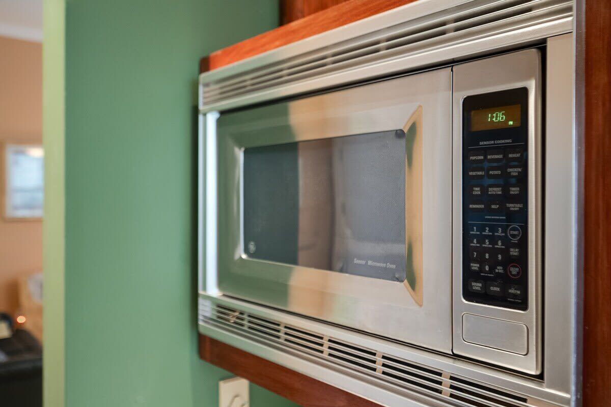 A microwave with a digital display and control panel, mounted on a wall with a wooden trim.
