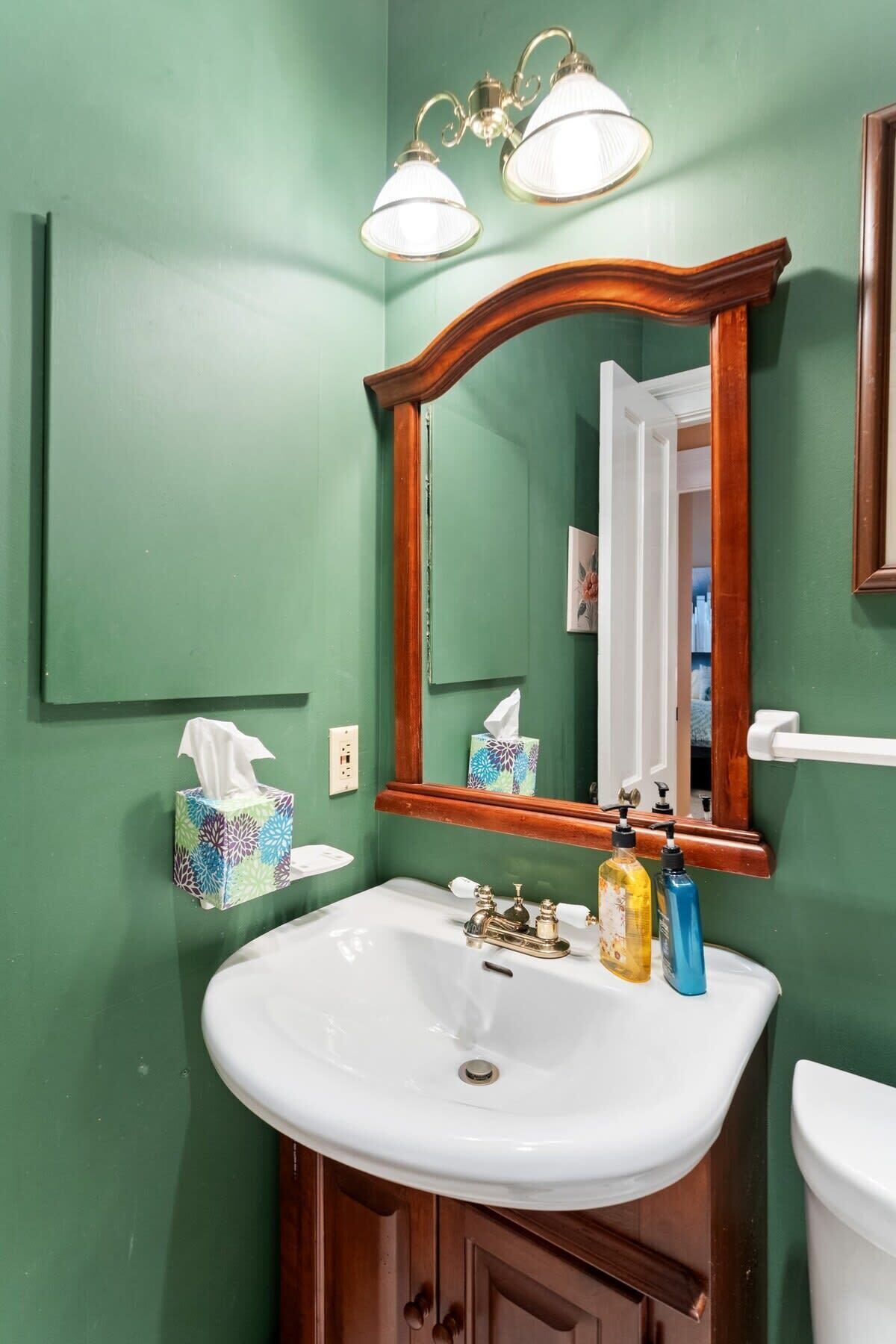 A bathroom with green walls, a white sink, a mirror, and two wall-mounted lights.
