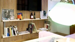A room with a wooden panel wall, a flat-screen TV mounted above a shelf with books and a bottle, and a desk with a lamp. - CloClo House: Design & Vintage above Metro: Nolo Area (Milano)